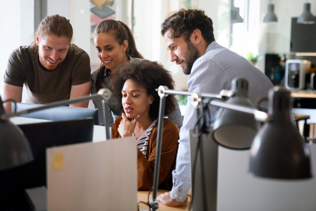 Ein Team von jungen Fachkräften diskutiert an einem Computer in einem modernen Büro.